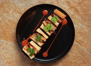 Grilled paneer skewers garnished with fresh herbs and served with signature sauce on a black plate.