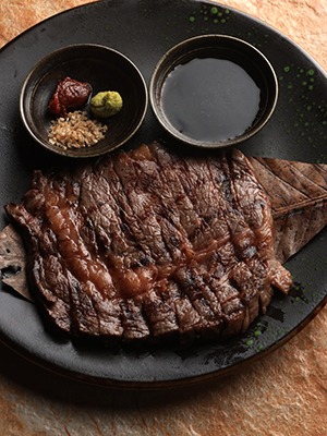 Wagyu steak served on a black plate with dipping sauces