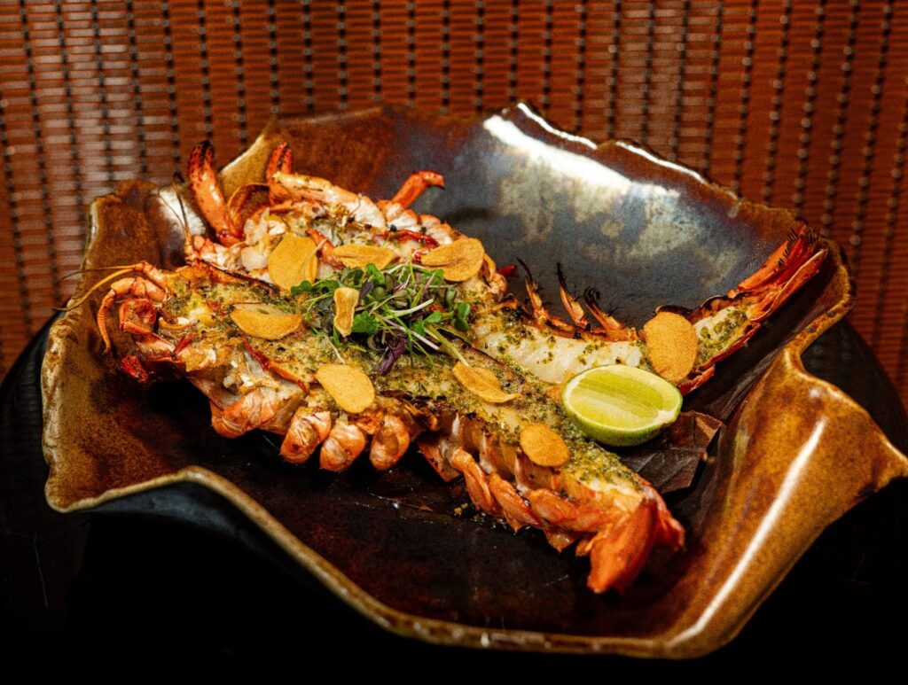 Josper baked whole Maine lobster served with chili ponzu butter sauce, crispy garlic chips, herbs, and lime