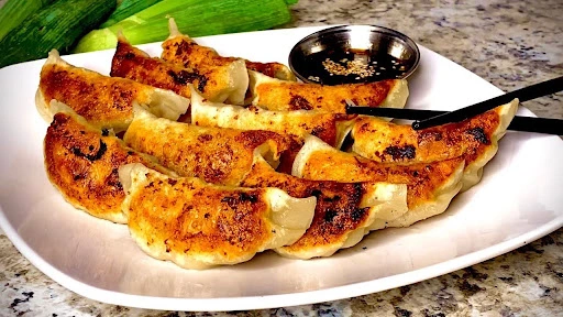 Pan-fried gyoza dumplings on a white plate with dipping sauce and chopsticks, garnished with scallions.
