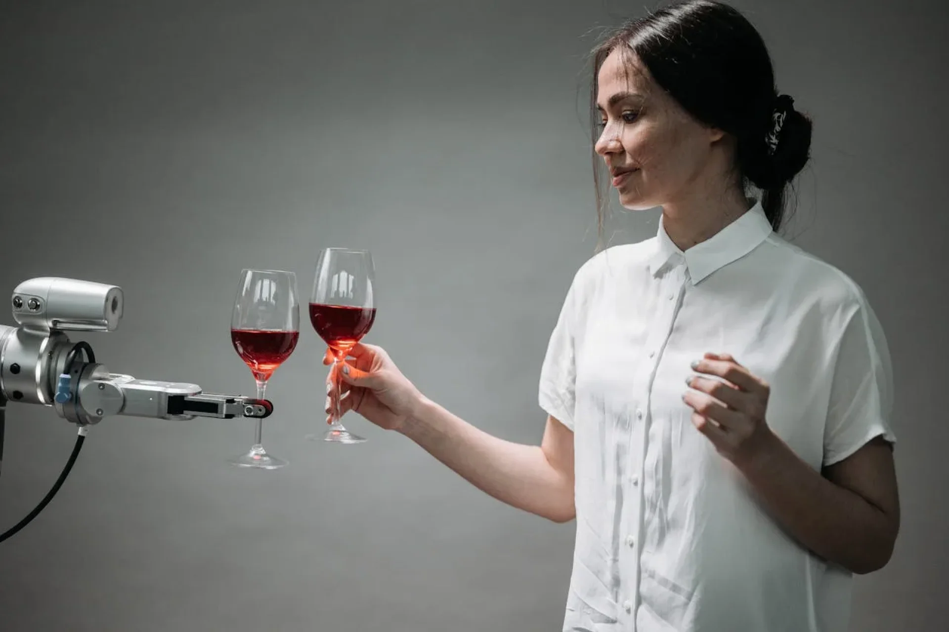 A woman holding a wine glass with a machine holding the other one