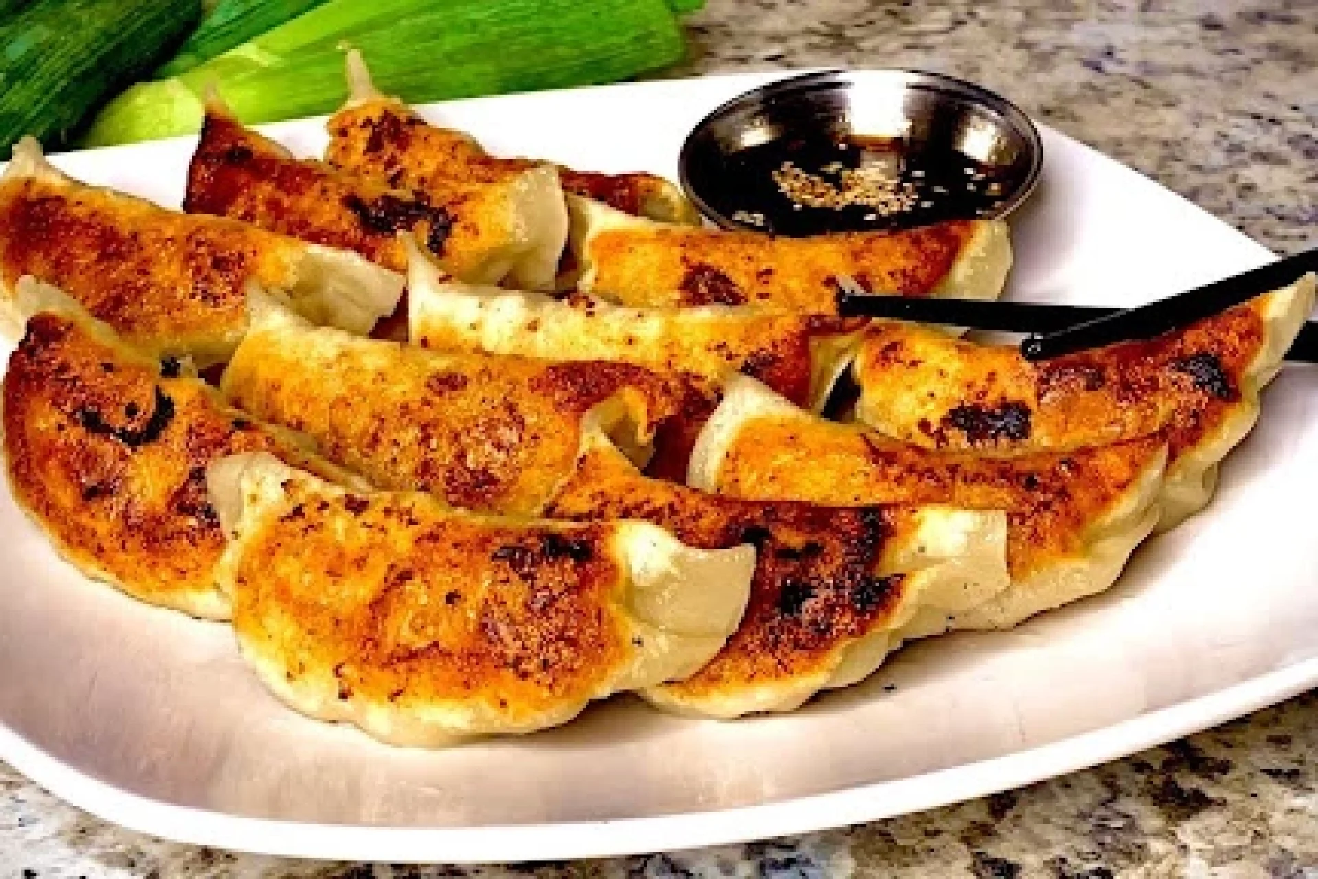 Pan-fried gyoza dumplings on a white plate with dipping sauce and chopsticks, garnished with scallions.